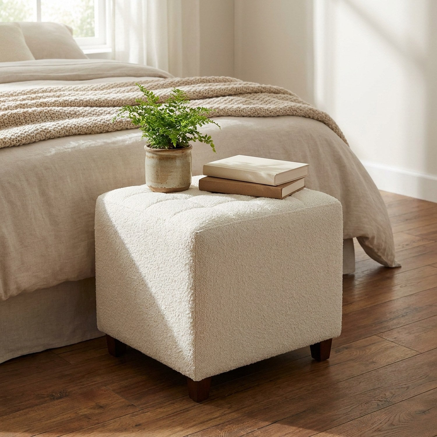 Pouf bouclé blanc à côté d'un lit avec une plante et des livres posés dessus