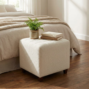 Pouf bouclé blanc à côté d'un lit avec une plante et des livres posés dessus