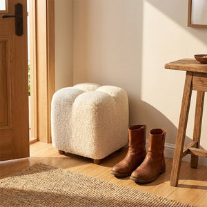 Pouf bouclé blanc dans une entrée près de bottes en cuir et d'une console en bois