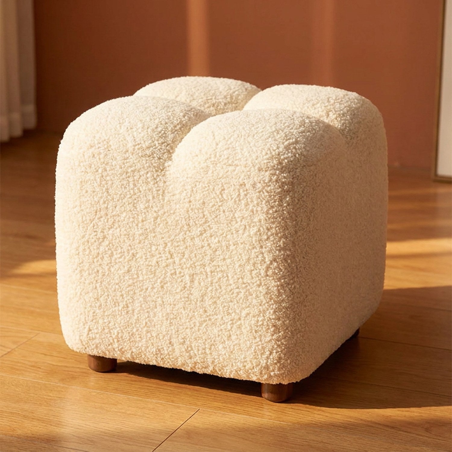 Petit pouf cube en tissu bouclé effet laine d'agneau blanc posé sur un parquet chaleureux