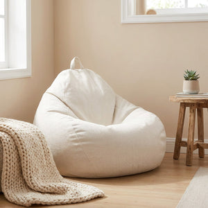 Pouf poire blanc cassé dans une chambre lumineuse avec plaid en maille et guéridon en bois