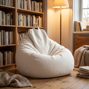 Pouf poire blanc cassé dans un coin lecture cosy avec bibliothèque en bois et lampadaire