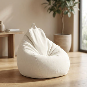 Pouf poire en coton et lin blanc cassé posé dans un salon lumineux avec plante et étagère