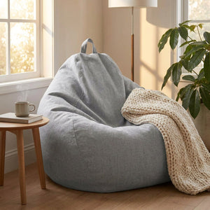 Pouf poire gris clair dans un coin lecture avec un plaid et une tasse pres d une fenetre