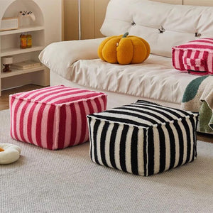 Pouf rayé noir et rose côte à côte devant un canapé