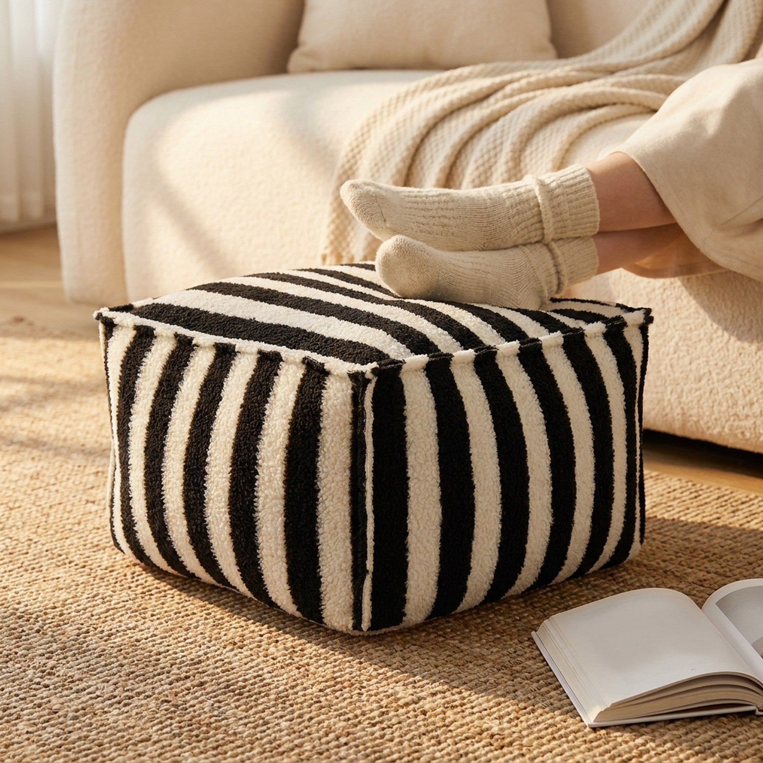 Pouf rayé noir utilisé comme repose pieds devant un canapé cocooning