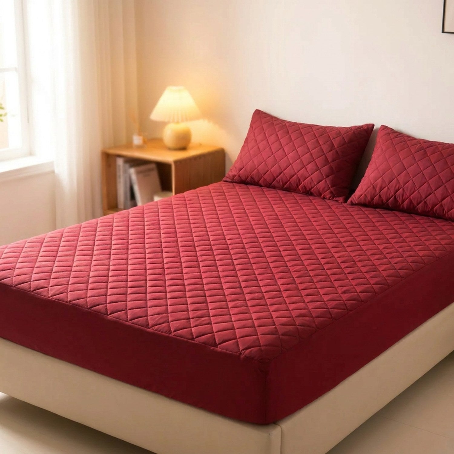 Protège matelas imperméable matelassé bordeaux posé sur un lit avec deux oreillers assortis