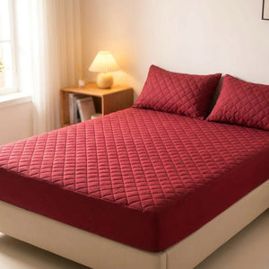 Protège matelas imperméable matelassé bordeaux posé sur un lit avec deux oreillers assortis