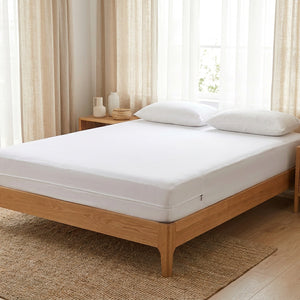 Protège-matelas blanc en place sur un lit dans une chambre scandinave lumineuse