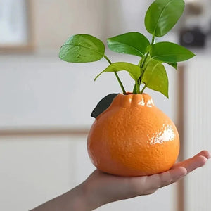 Vase en céramique en forme d'orange tenu dans la main avec une plante verte