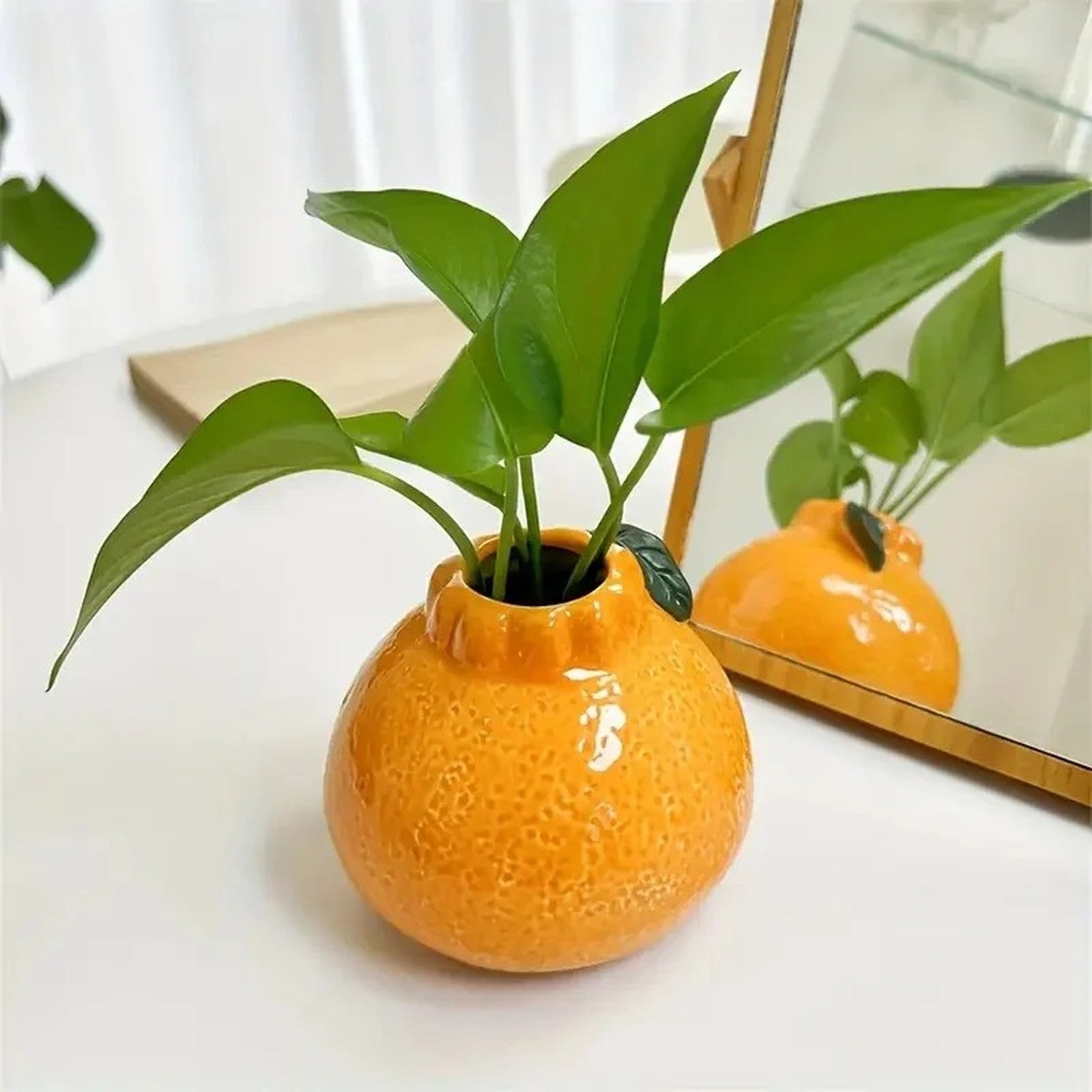 Vase en forme d'orange posé sur une table avec une plante verte
