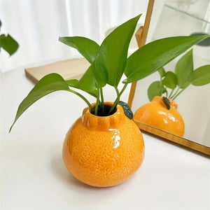 Vase en forme d'orange posé sur une table avec une plante verte