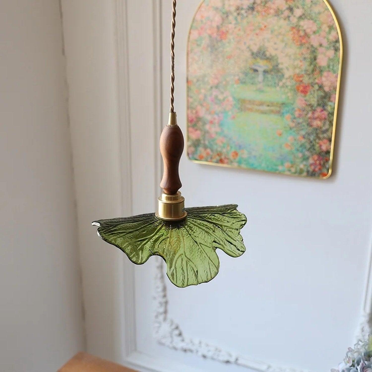 Suspension feuille en verre vert et bois de noyer devant un cadre fleuri