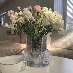 Vase en verre rayé design tulipe avec œillets blancs et roses dans intérieur lumineux