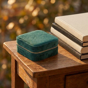 Boîte à bijoux velours vert foncé fermée sur table en bois avec livres lumière dorée