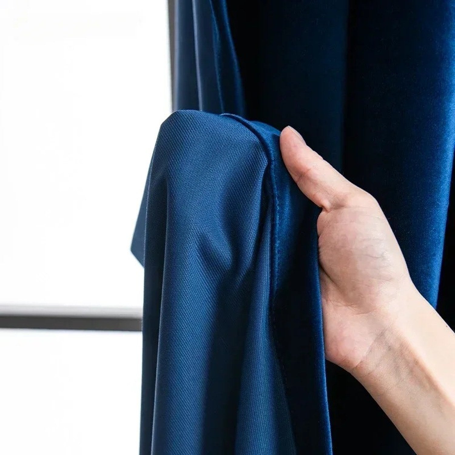 Détail du tissu velours bleu roi épais tenu à la main devant une fenêtre