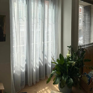Rideau voilage blanc devant une fenêtre avec une plante verte sur l'appui