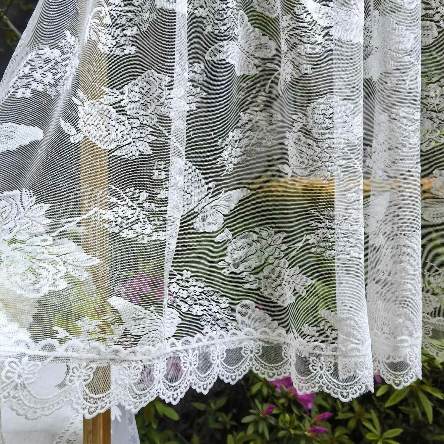 Détail du tissage en dentelle du rideau voilage montrant le motif fleurs et papillons