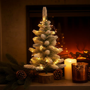 Sapin de Noël 45cm floqué de neige posé sur une cheminée avec bougies et pommes de pin