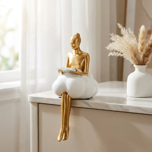 Sculpture femme dorée assise sur nuage blanc sur surface en marbre près d'une fenêtre
