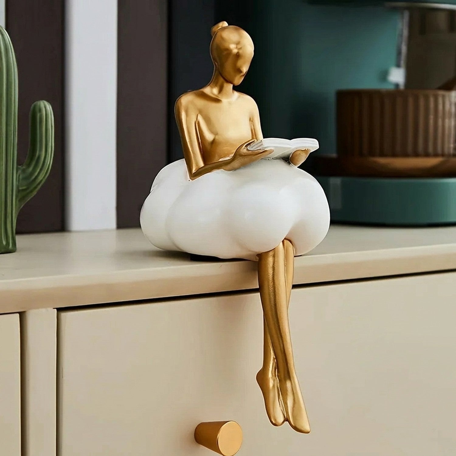 Figurine lectrice en résine dorée posée sur meuble avec livres et plante décorative