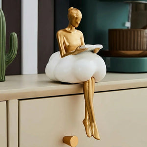 Figurine lectrice en résine dorée posée sur meuble avec livres et plante décorative