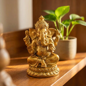 Figurine Ganesha en résine dorée posée sur une étagère en bois dans un intérieur chaleureux