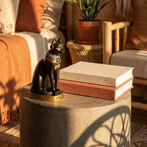Statuette chat Bastet noire sur table béton avec livres lumière dorée