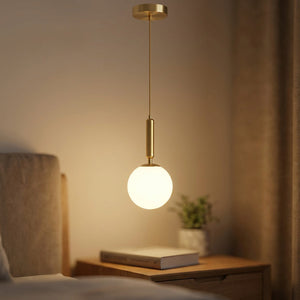 Suspension boule de verre dépoli en laiton allumée près d'un lit comme lampe de chevet dans une chambre cosy