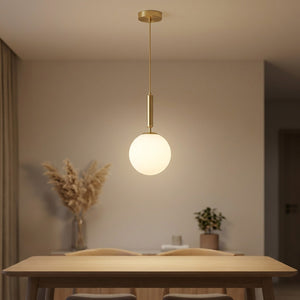 Suspension boule de verre dépoli blanc avec cordon en laiton allumée au-dessus d'une table dans un salon moderne