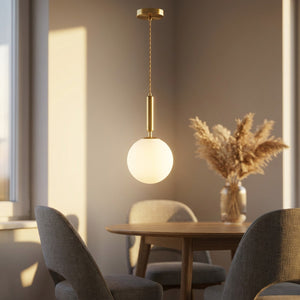 Suspension boule de verre dépoli en laiton allumée au-dessus d'une table à manger ronde dans une ambiance chaleureuse