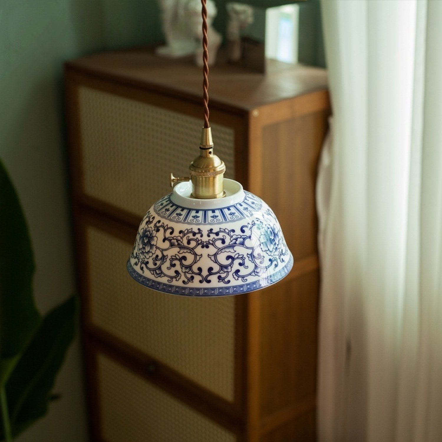 Suspension céramique motif bleu suspendue dans un salon vert avec commode en bois