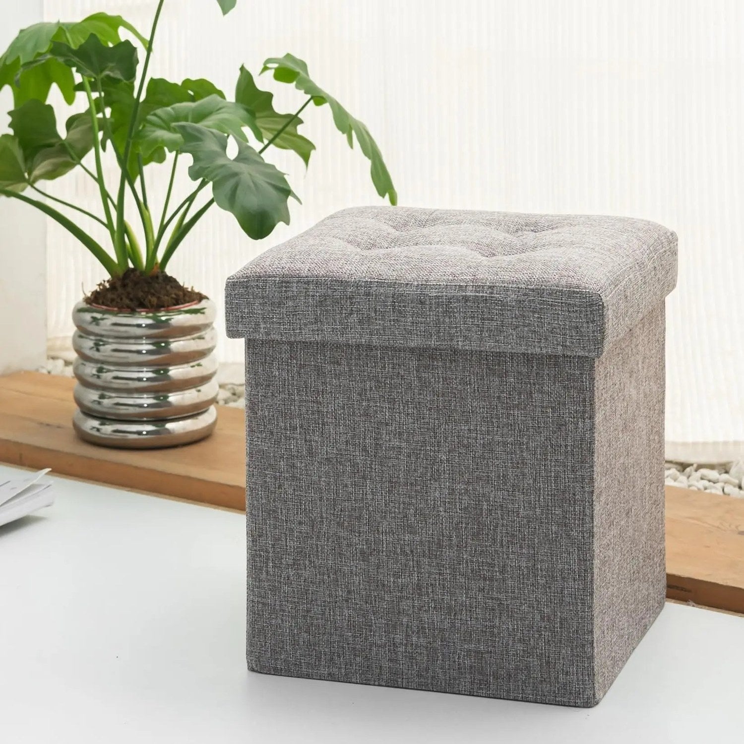 Tabouret gris coffre de rangement posé près d'une plante verte