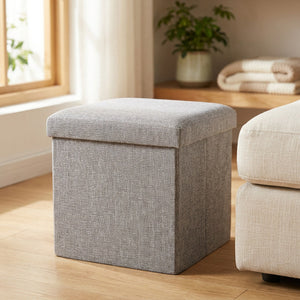 Tabouret de rangement pliable gris en tissu avec assise capitonnée posé dans un salon lumineux
