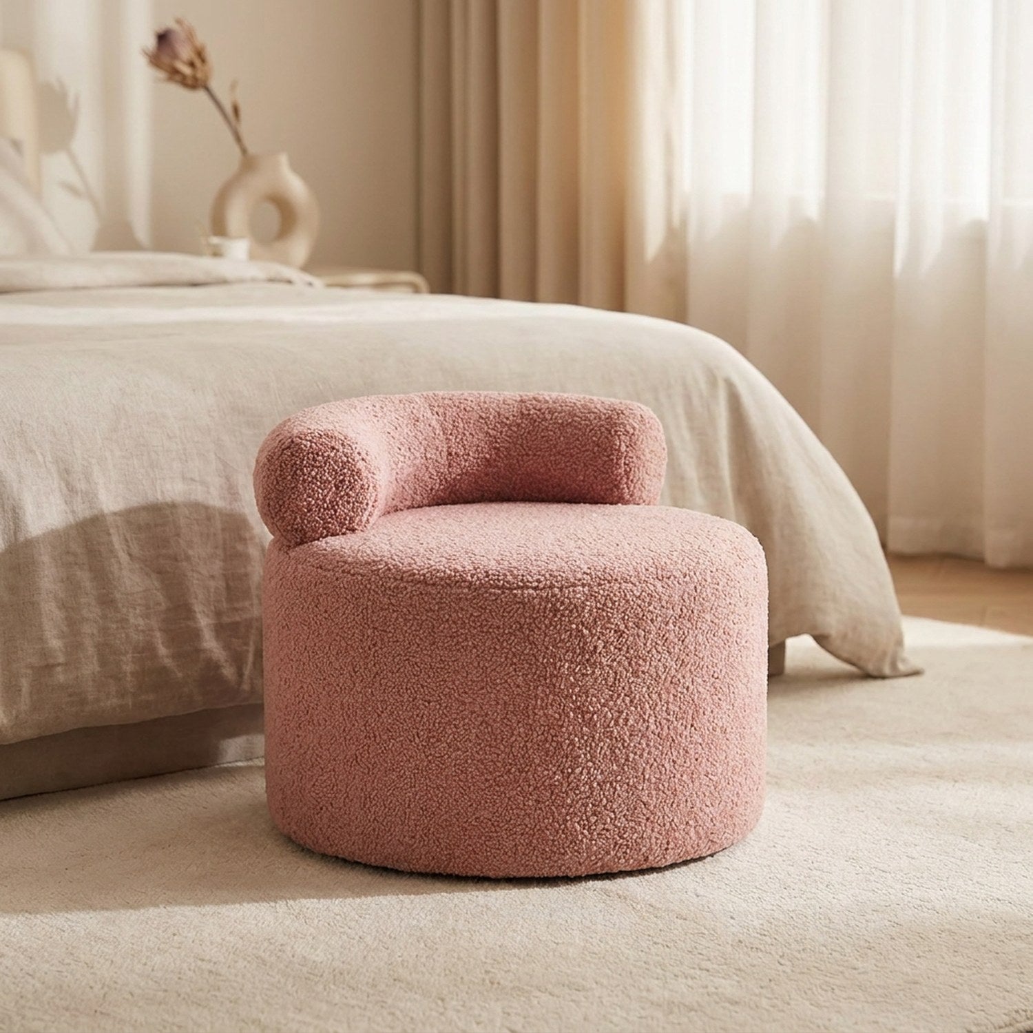 Tabouret pouf rond en bouclette rose poudré au pied d'un lit dans une chambre lumineuse
