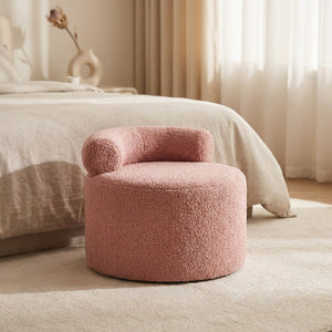 Tabouret pouf rond en bouclette rose poudré au pied d'un lit dans une chambre lumineuse