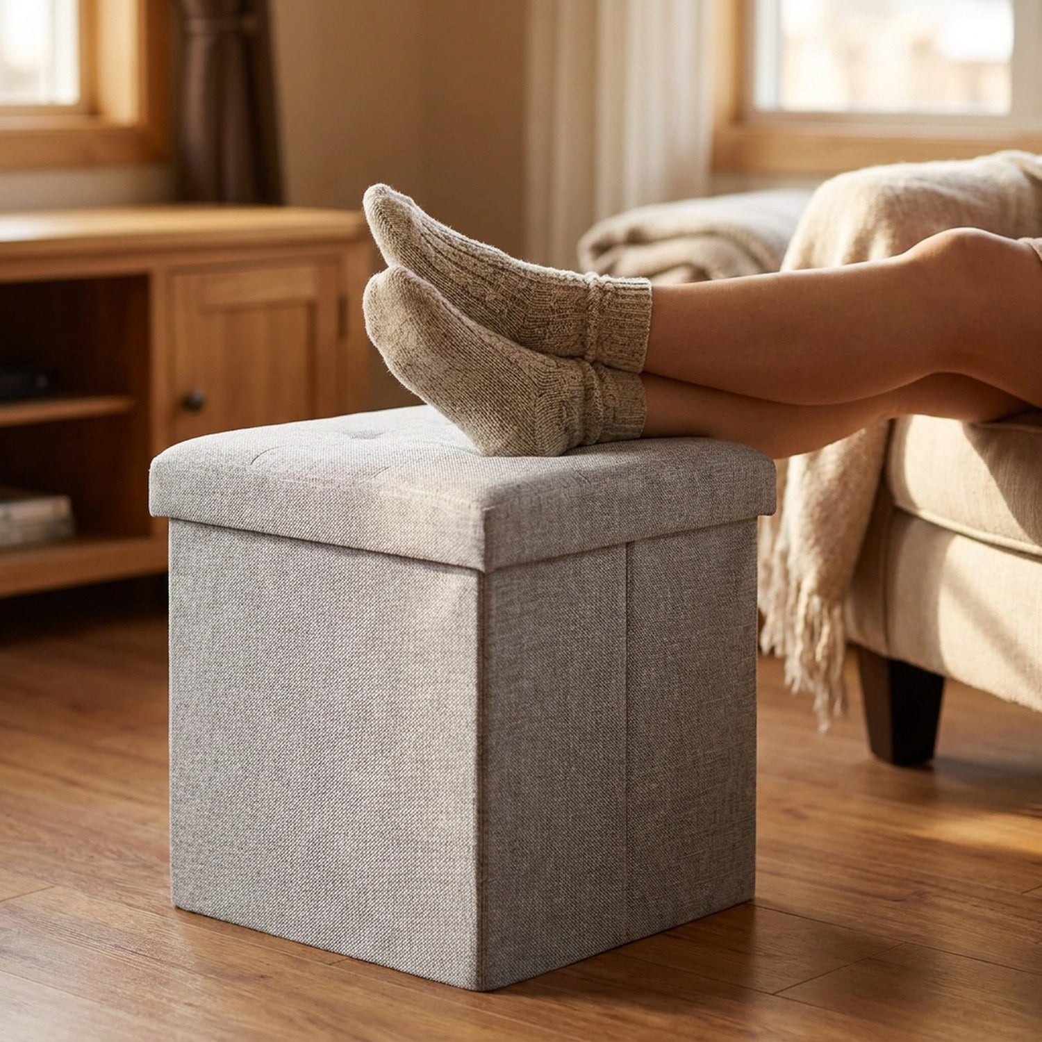 Tabouret de rangement gris utilisé comme repose-pieds à côté d un fauteuil
