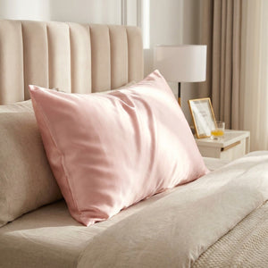 Taie d'oreiller en satin effet soie rose poudré posée sur un lit