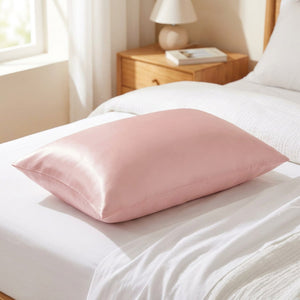 Taie d'oreiller en satin rose soyeux posée sur un lit clair dans une chambre lumineuse