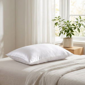 Taie d'oreiller en satin blanc sur un lit près d'une fenêtre lumineuse avec une plante