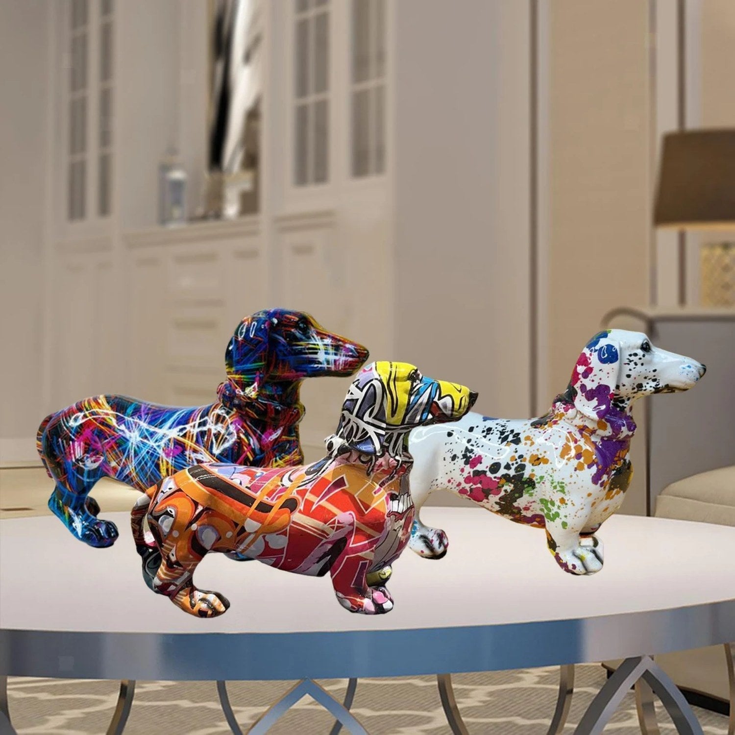 Trois statues teckel en résine avec motifs graffiti colorés posées sur une table basse de salon