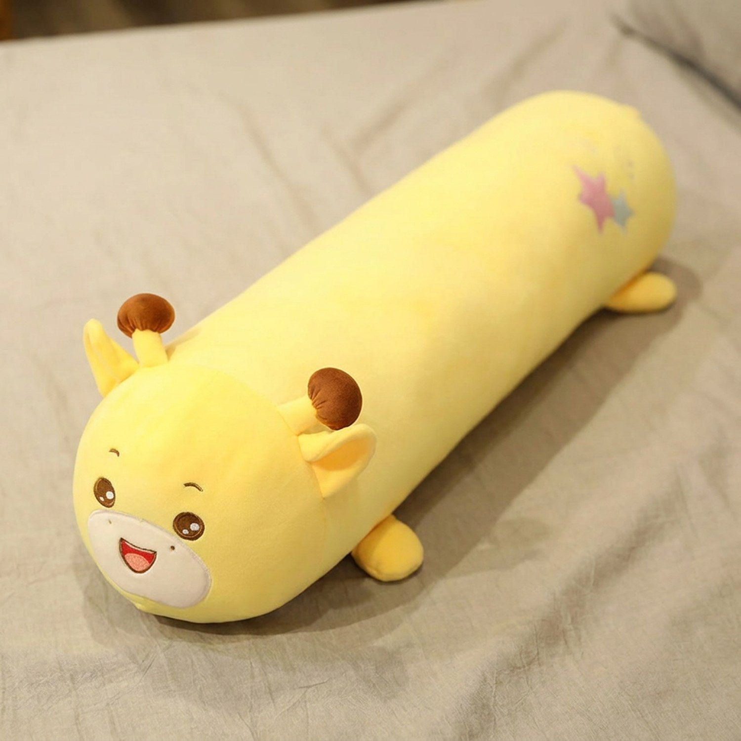 Traversin peluche en forme de girafe kawaii posé sur un lit clair