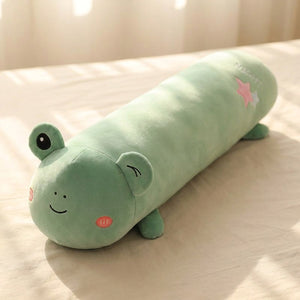 Traversin peluche en forme de grenouille kawaii posé sur un lit clair