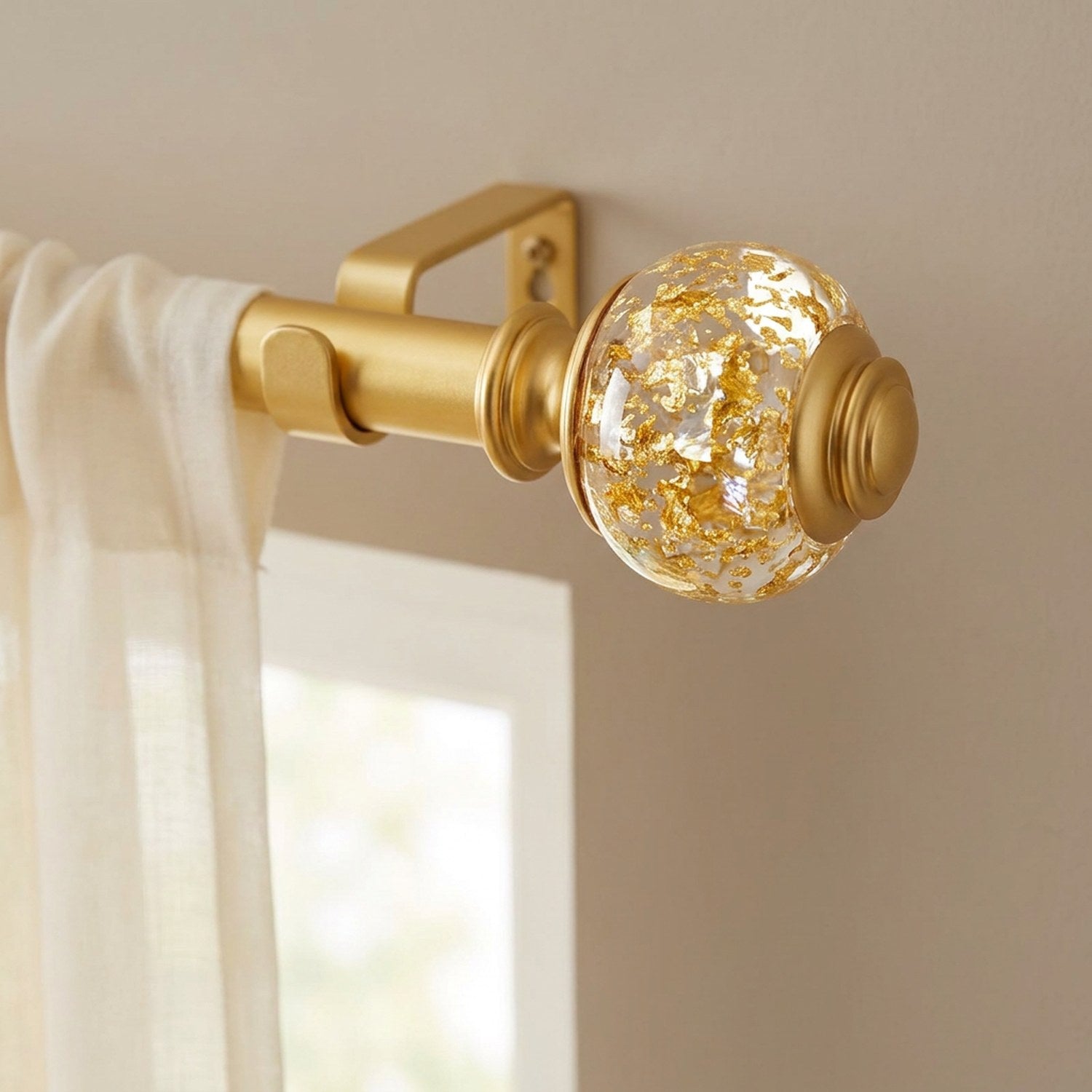Tringle à rideaux dorée avec embouts boule à feuille d'or installée au-dessus d'une fenêtre habillée de voilages