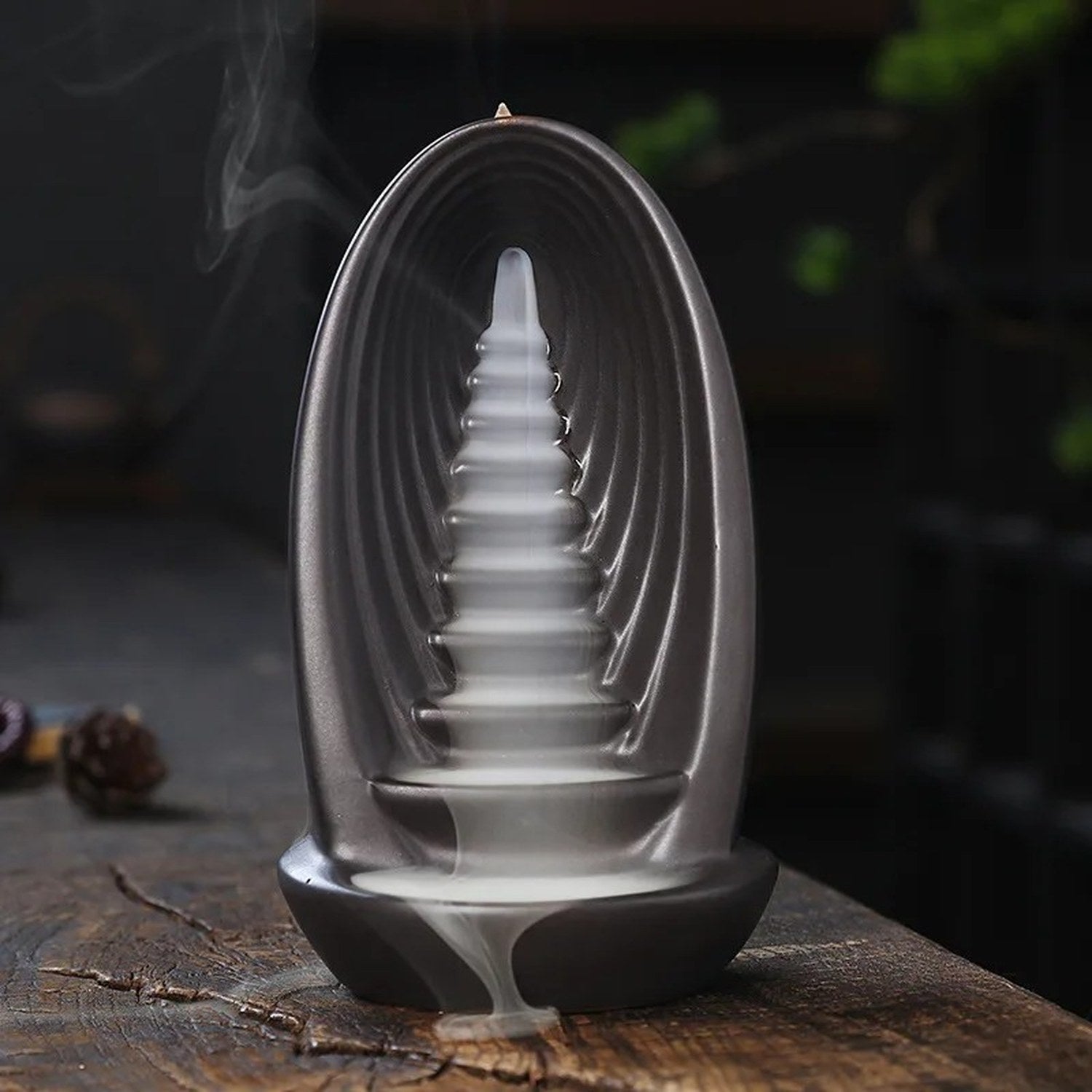 Brûleur d'encens à reflux en céramique vu de trois quarts avec fumée cascadant sur une table en bois