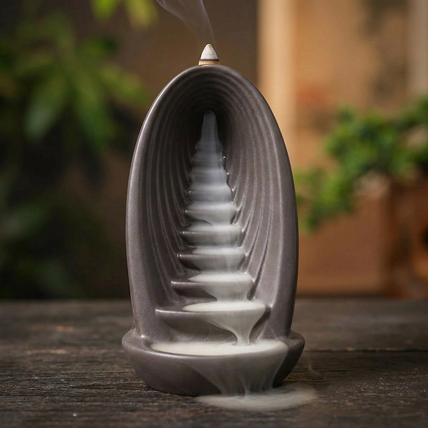 Brûleur d'encens à reflux en céramique grise avec fumée blanche cascadant le long des marches dans une ambiance zen