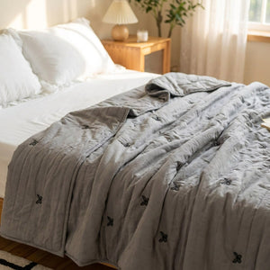 Couette d'été grise brodée de papillons sur un lit chaleureux