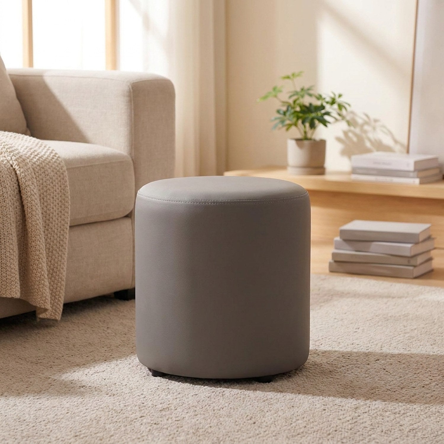 Tabouret pouf rond gris posé sur un tapis près d'un canapé beige