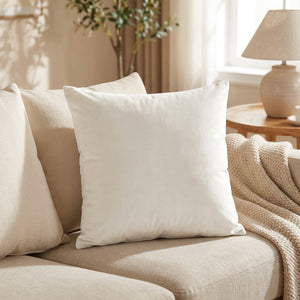 Housse de coussin en velours blanc cassé posée sur un canapé en lin clair
