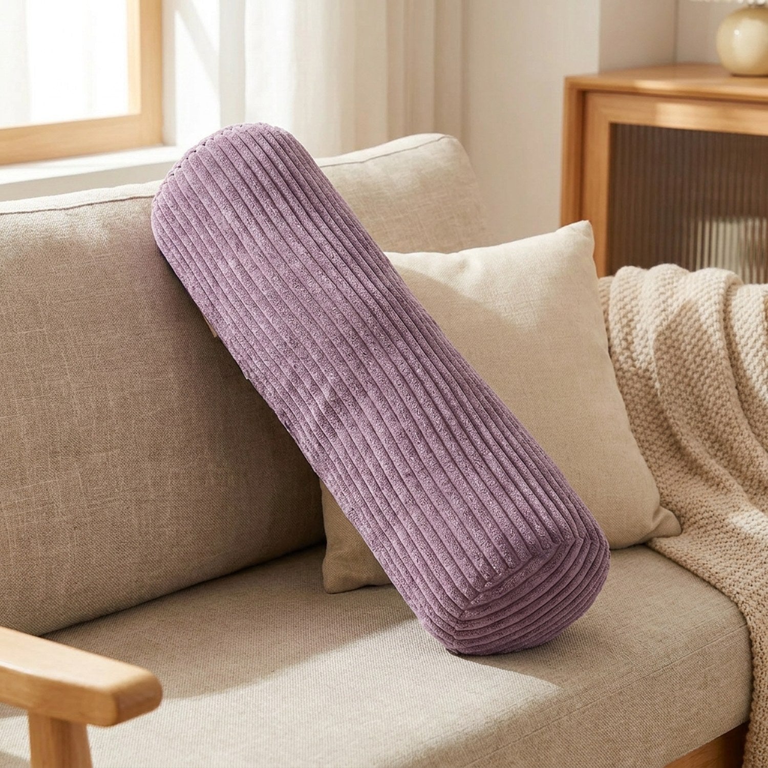 Traversin cylindrique en velours côtelé violet sur un canapé beige